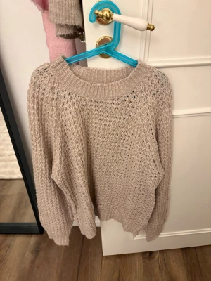 Beige stickad tröja från 157 - Säljer en beige stickad tröja från 157 med grovstickat mönster och rund halsringning. Tröjan har långa ärmar och ribbade muddar vid hals, ärmslut och nederkant. Perfekt för lager på lager och riktigt mysig att bära.