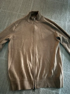 Morris zip-tröja - Snygg beige ziptröja med hög krage och hel dragkedja framtill. Tröjan har ribbade muddar vid ärmslut och nederkant, samt en stilren och enkel design som passar till det mesta. Tröjan består av 10% cashmere och 90% merinoull och tröjan produceras inte längre vilket gör den sällsynt. Priset är INTE hugget i sten!