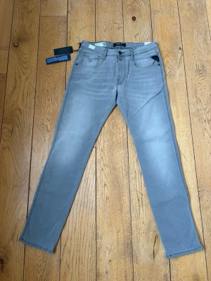 Replay Anbass - Snygga ljusblå jeans från Replay i slim fit-modell. Jeansen har klassisk femficksdesign, svarta detaljer vid fickan och subtila slitningar framtill. Tillverkade i mjukt denimtyg med stretch för extra komfort. Perfekta för en avslappnad och trendig look.