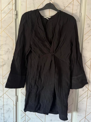 Svart klänning från H&M - Svart omlottklänning  från H&M i lätt, skrynkligt tyg. Klänningen har v-ringning, twistad knytning detalj framtill och trekvartsärmar. 