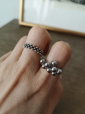 Silvriga pärlringar 925 stämpel pläterad  - Två coola ringar i silverfärgad metall, båda med pärlformade detaljer. Den ena ringen har små pärlor runt hela bandet, medan den andra har större pärlor i ett kluster. Perfekt för dig som gillar unika accessoarer och vill sticka ut.