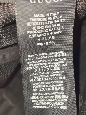 Gucci keps med orm och GG-mönster - Snygg svart keps från Gucci med klassiskt GG-mönster och en röd, vit och svart orm tryckt på framsidan. Tillverkad i Italien av polyuretan, bomull och polyester. Perfekt för dig som vill sticka ut med en exklusiv accessoar.