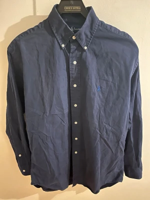 Ralph Lauren - Riktig snygg  mörkblå Ralph Lauren skjorta som passar både till vardag och fest.Fint skick. Inga skador eller fläckar. Kan såklart diskutera pris för en snabb affär. 