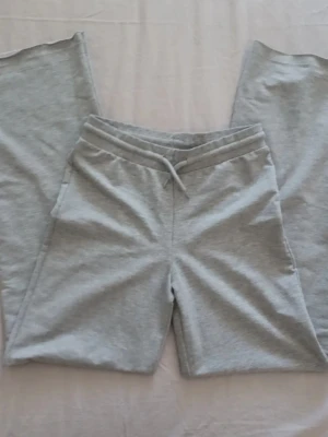 Ljusgrå mjukisbyxor med dragsko - Säljer ett par ljusgrå mjukisbyxor med resår i midjan och justerbar dragsko. Byxorna har raka ben och är tillverkade i mjukt sweatshirtmaterial, perfekta för chill dagar. Inga synliga loggor eller märken. Är I stl 160 men passar mug som använder xs. Har sprättat upp byxorna så att de skulle "bli längre" vilket inte gjorde en stor skillnad men annars är de i bra skick. 