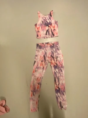 Färgglatt träningsset med mönster - Säljer ett sportigt träningsset med matchande crop top och tights. Setet har ett abstrakt mönster i rosa, lila, svart och vitt. Materialet är stretchigt och passar perfekt för gym eller yoga. Midjehöga tights och topp med breda axelband.