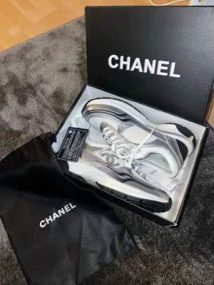 Chanel runner - Snygga Chanel sneakers i vitt och silver med metallicdetaljer och tydlig logga på sidan. Skorna har chunky sula, vita skosnören och meshpaneler för extra komfort. Perfekta för dig som vill ha en exklusiv och trendig look. Storlek 41