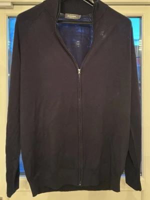 Mörkblå merinoullskofta Dressmann - Stilren mörkblå kofta från Dressmann i mjuk merinoull. Koftan har hel dragkedja framtill, ribbad krage och muddar. Perfekt för lager på lager och enkel att matcha med olika outfits.