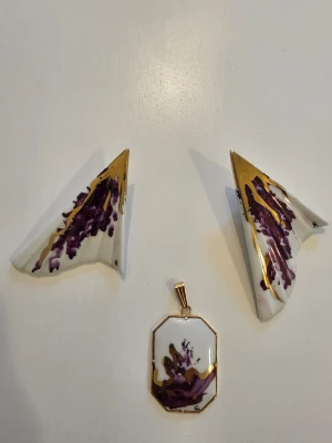 Vita och lila geometriska örhängen - Unika örhängen i vit keramik med geometrisk form, dekorerade med abstrakta lila och guldiga detaljer. Klämfäste på baksidan. Perfekta för dig som vill sticka ut med konstnärliga accessoarer.