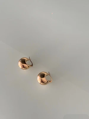 Chunky guldfärgade hoops örhängen - Säljer ett par chunky hoops örhängen i guldfärg. De har en rund, bullig form och en blank, spegelblank yta som ger en modern och trendig look. Perfekta för dig som gillar statement-smycken och vill addera lite extra bling till din stil. Aldrig använt, i nyskick. 