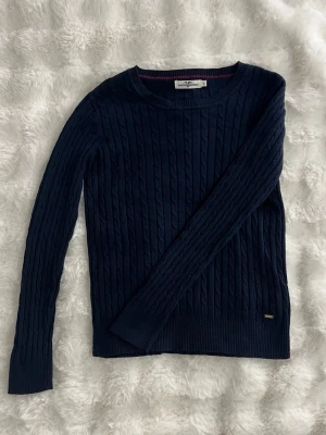 Mörkblå kabelstickad tröja  - Snygg mörkblå kabelstickad tröja från Gant med rund halsringning och ribbade muddar. Tröjan har ett diskret metallmärke vid nederkanten och är perfekt för lager på lager. Klassisk och tidlös design som passar till det mesta. Inga defekter förekommer. Bild med plagget på kan skickas vid begäran. Postar inom 1-2 dagar. Pris kan diskuteras.  Finns även ute på min vinted:ellyssellout