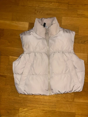 Beige dunväst från H&M Divided - Beige dunväst från H&M Divided med hög krage och dragkedja framtill. Västen har två fickor på sidorna och en puffig design. Pris kan diskuteras 😊