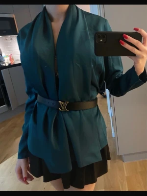 Mörkgrön blus med lös passform - Stilren mörkgrön blus med avslappnad, öppen design och bred krage. Kavajen har en mjuk, flowy känsla och kan stylas med bälte för markerad midja. Perfekt till lager-på-lager och trendiga outfits.