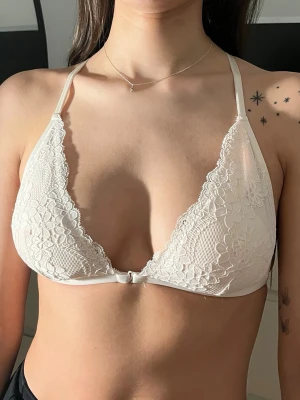 Ljusrosa spetsbralette med snörning bak - Säljer en vit bralette i spets med triangelformade kupor och tunna axelband. Framtill har den djup urringning och baktill finns snygg snörningsdetalj i spets. Justerbara band för bästa passform. Perfekt för dig som gillar en feminin och trendig look.
