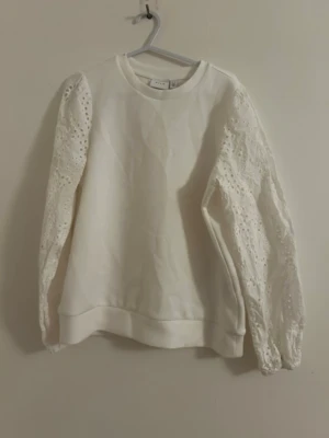 Vit sweatshirt med spetsärmar - Supersnygg vit sweatshirt från Gina Tricot med unika spetsärmar i broderad design. Tröjan har rund halsringning och ribbade muddar. Perfekt för dig som vill ha en basic tröja med en twist. Materialet är mjukt och bekvämt, och spetsdetaljerna ger en romantisk vibe.