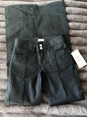 Svarta bootcut jeans från Nelly - Snygga svart bootcut jeans från nelly med pressveck framtill och dubbla knappar i midjan. Jeansen har klassiska fem fickor och coola detaljer på bakfickorna. Materialet är stretchigt och ger en skön passform. Perfekta för en trendig och avslappnad look.