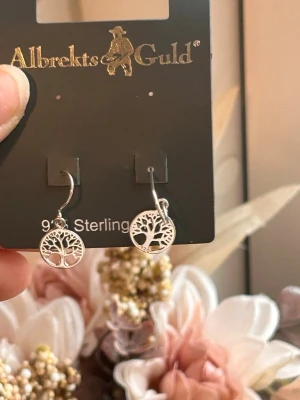 Silvriga örhängen Livets träd - Snygga örhängen i äkta silver från Albrekts Guld med ett detaljerat Livets träd-motiv. Hängande modell med rund form och öppen design som ger en stilren och modern känsla. 