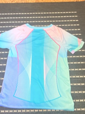 Barça x Nike pastell matchtröja - Snygg FC Barcelona matchtröja i pastellfärger med blå, rosa och vita toner. Tröjan har korta ärmar, V-ringning och tryckta loggor från Nike, Spotify och Barça. Tillverkad i lätt och ventilerande funktionsmaterial, perfekt för träning eller match. 