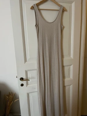 Beige ribbad maxiklänning - Lång ribbad klänning i beige med breda axelband och rundad urringning. Klänningen har en rak och smickrande passform och är gjord i ett mjukt, stretchigt material som känns bekvämt mot huden. Perfekt för en avslappnad och stilren look.