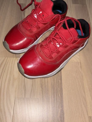 Jordan 11 low Red  - Snygga röda sneakers från Jordan med vita detaljer och svart insida. Skorna har lågt skaft, röda skosnören och en vit sula med grå förstärkning vid tån. Ovandelen är i syntetmaterial och mesh för bra andningsförmågar.