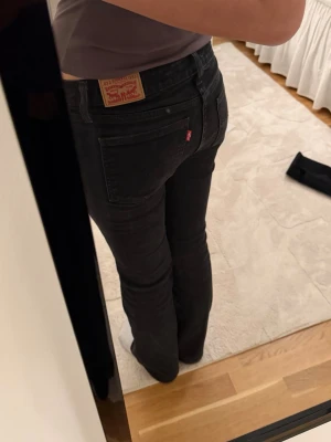 Svarta bootcut jeans från Levi's - Snygga svarta jeans från Levi's med klassisk femficksmodell och bootcut passform. Jeansen har en diskret tvätt och den ikoniska röda Levi's-lappen på bakfickan. Perfekta för dig som gillar en tidlös och avslappnad stil.