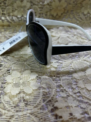 Svarta och vita cat eye solglasögon - Snygga solglasögon i cat eye-modell med svart front och vita bågar. Glasen är mörka och ger ett coolt uttryck. Perfekta för att lyfta din stil under soliga dagar.