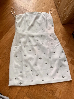 Vit kort klänning  - Snygg vit kort klänning med silverfärgade blommiga detaljer framtill. Klänningen har en rak passform och är perfekt för sommarens alla tillfällen. Baksidan har en smockad panel för extra komfort.Skriv gärna för mått! 💕
