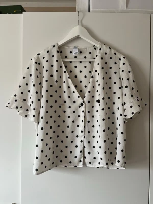 Vit prickig blus med v-ringning - Snygg vit blus som har knappar som även kan justeras på två olika sätt! 