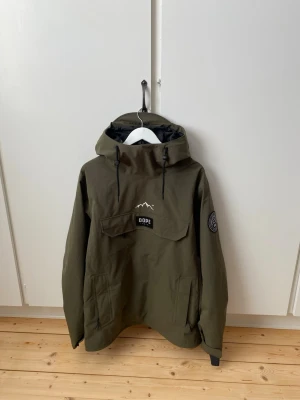 DOPE Blizzard Snowboardjacka - Snowboardjacka från Dope - modellen ”Blizzard olive green” i storlek L herr (lite oversized & rymlig passform). - vattentät och lätt skidjacka i pullover-stil.  • ”Skaljacka”- Ingen vaddering, ser till så plagget är lätt och mångsidigt. Använd lager för att anpassa efter väder.  • Stormsäker huva med dragskor fram och bak. • Ventilation under ärmarna. • Mediaficka och liftkortsficka. Skick: Använd ca 1-2 gånger men helt utan hål, märken och fläckar. Mycket fint skick alltså!  📦 Redo att skickas!