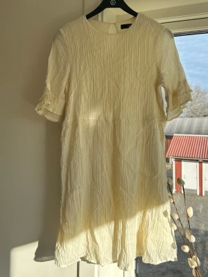 Ljus kort klänning med volangärm - Säljer en ljus, kort klänning med rund halsringning och volangdetaljer på ärmarna. Klänningen har en avslappnad passform och är perfekt för varma dagar.🌸