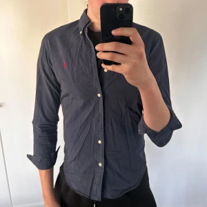 Ralph lauren skjorta  - En marinblå Ralph lauren skjorta i fint skick. Använd men inte mycket tecken på de. Perfekt till sommaren, i storlek S slimfit