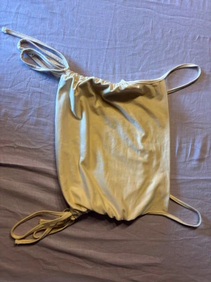 Beige croppad linnetopp med snörning - Trendig beige linnetopp med tunna axelband och snörning i sidorna för justerbar passform. Toppen är croppad och har en enkel, stilren look som passar perfekt till sommaren. Tillverkad i mjukt syntetmaterial för en skön känsla.