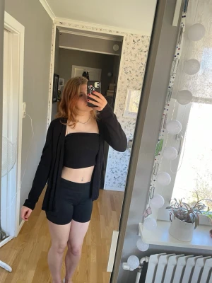 Svart öppen cardigan - En svart, långärmad öppen cardigan i mjukt och tunt material. Enkel och stilren design utan knappar eller dragkedja, perfekt att slänga över en topp. Passar till många olika outfits och har en avslappnad passform.