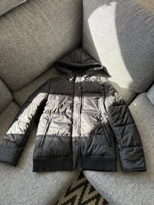 Moncler jacka - hysteric glamour  - Säljer en svart pufferjacka från hysteric glamour med huva och ribbade muddar. Jackan har dragkedja och tryckknappar framtill, två sidofickor och en bröstficka. Perfekt för kalla vinterdagar och riktigt snygg streetstil.