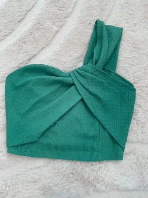 Grön one shoulder topp - Snygg grön topp med one shoulder-design och twistad detalj framtill. Använd fåtal gånger storlek s passar xs 