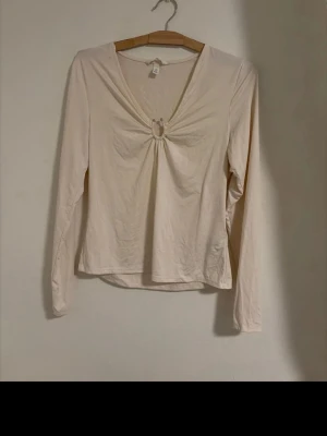 Vit långärmad topp med ringdetalj - Söt vit/beige långärmad topp med v-ringning och fin ringdetalj framtill.