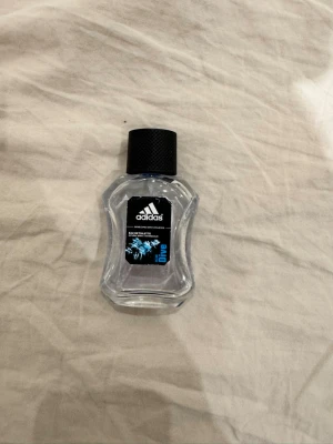 Adidas Ice Dive Eau de Toilette - Fräsch parfym från Adidas i modellen Ice Dive. Flaskan är transparent med en svart etikett och blå detaljer, och har en sportig, vågformad design. Korken är svart och har struktur för bättre grepp. Perfekt för dig som gillar en energisk och uppfriskande doft. Ungefär 35 ml kvar av 50 ml