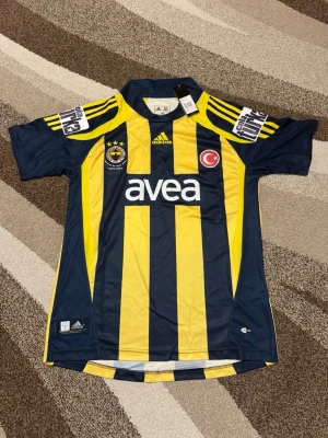 Fenerbahce 07-08 Hemmatröja  - Säljs av ICEKIT  Storlek: M Namn + nummer: Alex #10 Badge: Cola Turka  Här kan du se tröjor i ICEKIT Outlet. Alla tröjor är helt nya och utan några problem. Du kan välja att köpa dem här eller direkt via vår hemsida.  Tröjorna finns tillgängliga hos ICEKIT på: https://www.icekit.se  Länk: https://www.icekit.se/collections/outlet