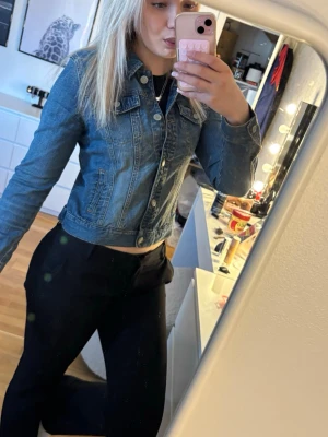 Klassisk blå jeansjacka - Snygg blå jeansjacka med figurnära passform och klassiska sömmar. Jackan har knäppning framtill, två bröstfickor med lock och krage. Perfekt att slänga över en t-shirt för en cool och avslappnad look.