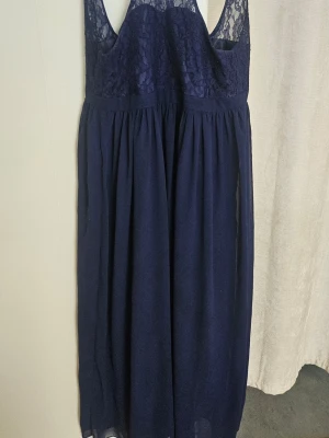 Marinblå långklänning med spets - Elegant marinblå långklänning med v-ringad spets upptill och ärmlös design. Kjolen är luftig och faller snyggt. Perfekt för speciella tillfällen när du vill känna dig extra fin.