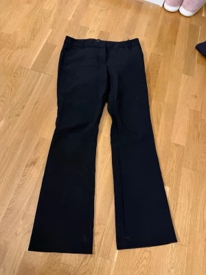 Svarta utsvängda kostymbyxor - Snygga svarta kostymbyxor med utsvängda ben och klassisk midja. Byxorna har en stilren look och passar perfekt till en dressad outfit. Materialet ser ut att vara en mjuk och följsam textil som ger en skön känsla. Inga synliga detaljer eller loggor.