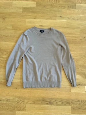 Beige rundhalsad tröja  - En stilren beige tröja med rund halsringning och ribbade muddar vid ärmslut och nederkant. Perfekt basplagg i garderoben, enkel att matcha och har en klassisk passform. Tillverkad i mjukt material för skön känsla. Skick 10/10
