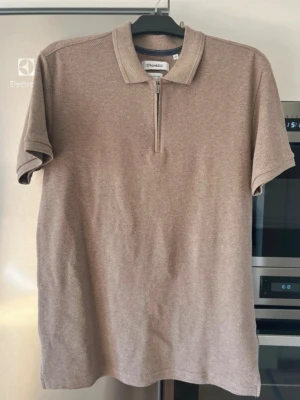Strömbergs T-shirt  - Säljer en beige topp från Stone Island med klassisk krage och half zip framtill. Toppen är kortärmad och har en normal passform. Materialet känns som bomull och ger en stilren look.
