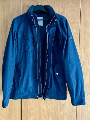 J.Lindeberg Jacka - Säljer en snygg och praktisk vår- och regnjacka från J.Lindeberg, Field Jacket. I superfint skick, inget att anmärka på. Nypris 2800kr. Finns en dold luva i kragen.