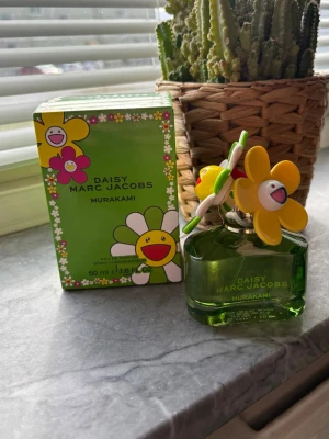 Daisy Marc Jacobs Murakami parfym - Daisy Marc Jacobs Murakami parfym med grön glasflaska och färgglada blomdetaljer på korken. Flaskan har en lekfull design med Murakami-blommor och kommer i en matchande grön kartong med glada blommor. Volymen är 50 ml. Ny