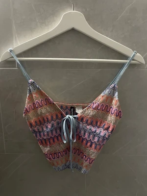 Färgglad linnetopp med snörning - Säljer en unik och färgglad linnetopp från Bershka med tunna blå axelband och snörning framtill. Toppen har ett vågigt mönster i rosa, blått, beige och orange.
