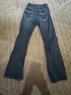 Blå bootcut jeans med kontrastsömmar - Säljer ett par blå bootcut jeans med snygga kontrastsömmar och broderade bakfickor. Jeansen har klassisk femficksdesign och normal passform. Perfekta för en avslappnad och trendig look.