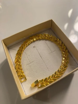 18K Guldpläterad Armband  - Snyggt armband i guldfärgad metall med detaljerat bladmotiv runt hela bandet. Armbandet har en platt och bred design som ger ett statement-intryck. Perfekt accessoar för att lyfta din outfit med en trendig touch.
