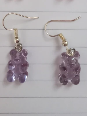 Lila björn örhängen - Säljer ett par unika örhängen med lila gummibjörns-hängen i plast. Örhängena har krokar i metall och är knappt använda. 