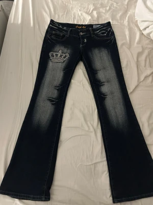 Mörkblåa bootcut jeans med kronor från crazy age - Snygga jeans från crazy age med kronor fint skick endast några glitter paletter som har lossnat💕 säljes eftersom de inte används längre. Innerbenslängden: 81cm midjemåttet: 39cm