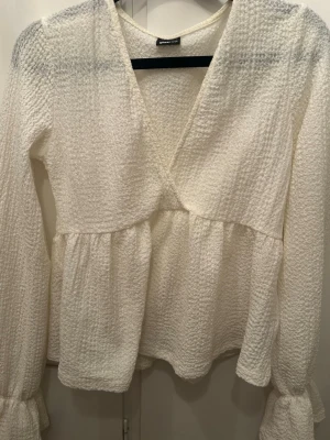 Vit omlottblus från Gina Tricot - Säljer en söt vit omlottblus från Gina Tricot i storlek S. Materialet är mjukt och stretchigt, vilket ger en skön passform, använd 3 gånger. 